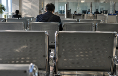 Waiting area in immigration office, man seated on metal chair facing service counter